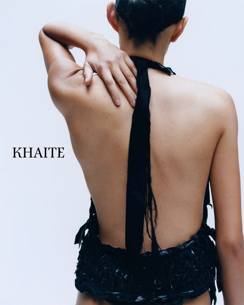 Model seen from behind wearing a black halter top with a long strap trailing down her back against a white background.