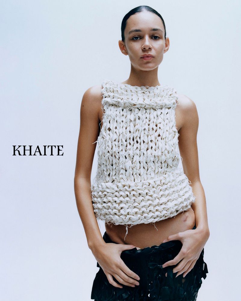 Model Binx Walton wearing a chunky white knit sleeveless top and dark skirt against a white studio background for Khaite S/S 2026.