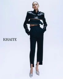 Model wearing a cropped black leather jacket and black trousers against a white seamless background