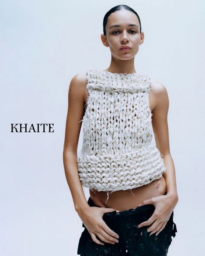 Model Binx Walton wearing a chunky white knit sleeveless top and dark skirt against a white studio background for Khaite S/S 2026.