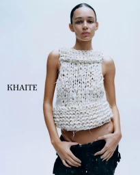 Model Binx Walton wearing a chunky white knit sleeveless top and dark skirt against a white studio background for Khaite S/S 2026.