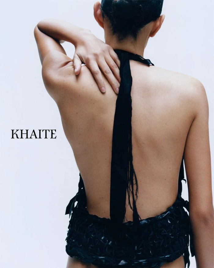 Model seen from behind wearing a black halter top with a long strap trailing down her back against a white background.
