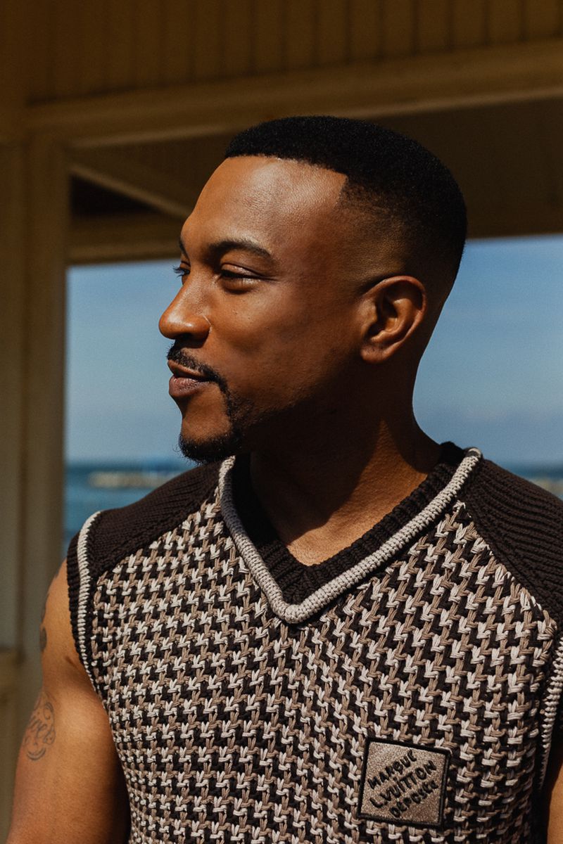 Close-up of an adult male with short dark hair, wearing a patterned vest, looking off to the side in an outdoor setting with natural light.