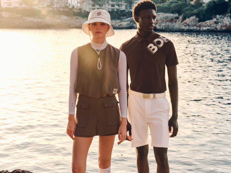 A man and a woman in golf apparel stand by the water at sunset for BOSS GOLF campaign.