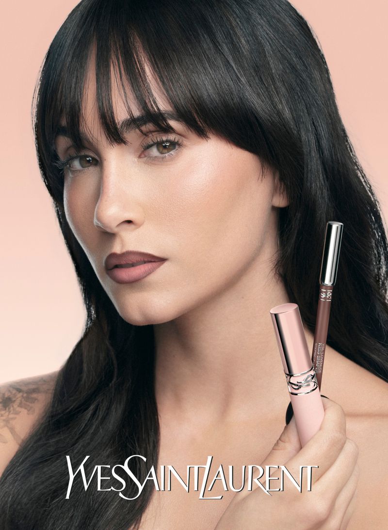 Close-up beauty shot featuring a woman with black hair and neutral makeup holding Yves Saint Laurent lipstick and eyeliner.