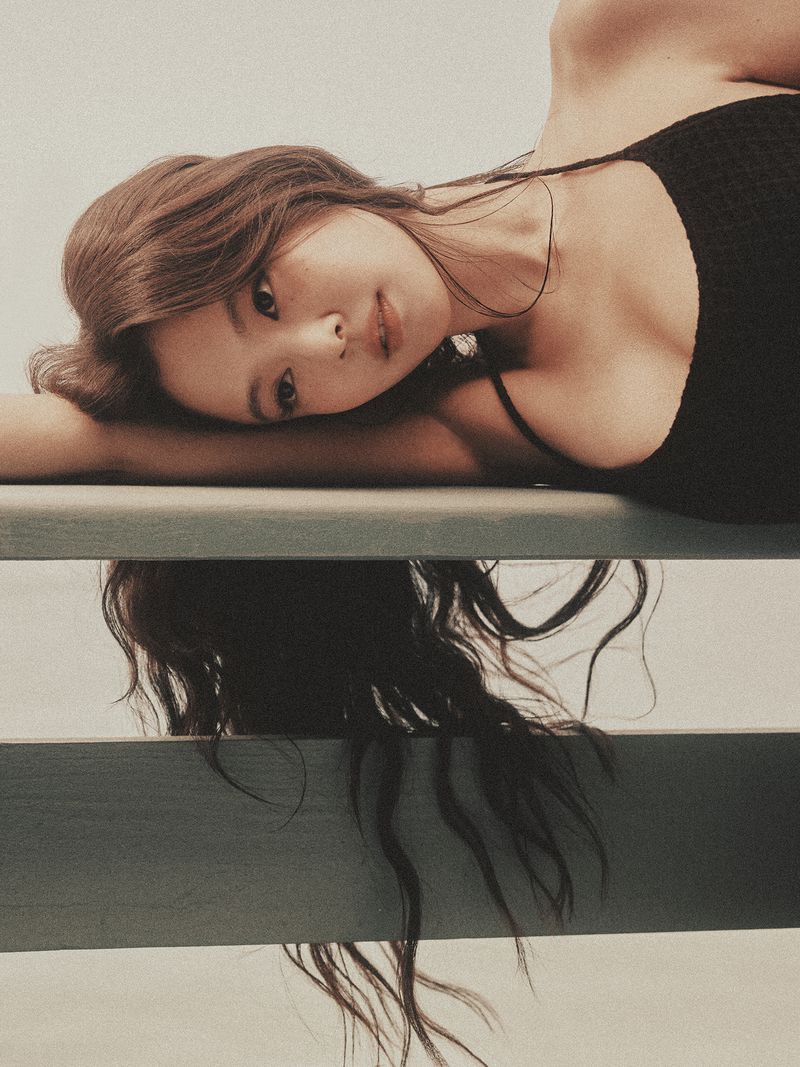 Jennie lying horizontally resting head on arms wearing black top with long dark hair hanging down
