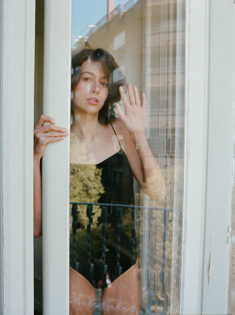 Woman in black bodysuit peering through a glass door with balcony reflections for Zara Lingerie by photographer Berta Pfirsich.