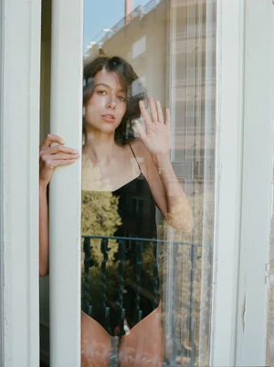 Woman in black bodysuit peering through a glass door with balcony reflections for Zara Lingerie by photographer Berta Pfirsich.