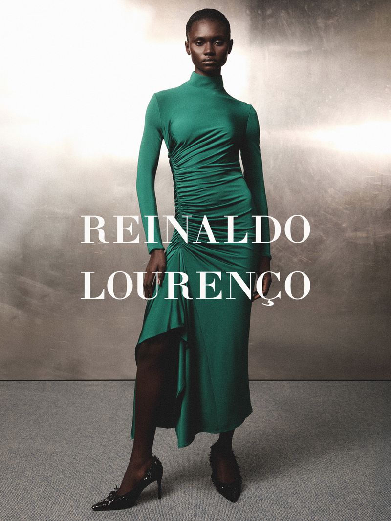 Model wearing a long-sleeved green dress standing against a textured metallic background with text overlay