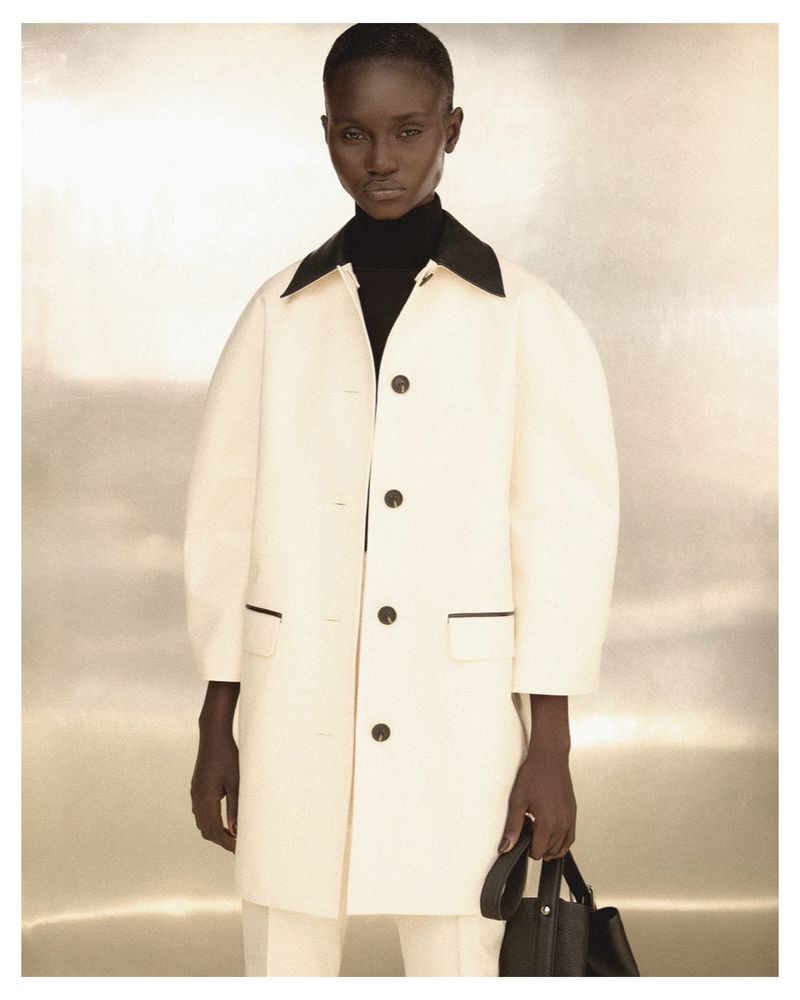 Model wearing a cream coat with black collar and dark turtleneck against a metallic backdrop for Reinaldo Lourenço A/W 2026.