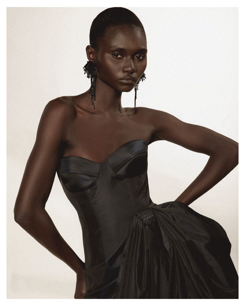 Model wearing a black strapless gown with textured black earrings against a plain white background