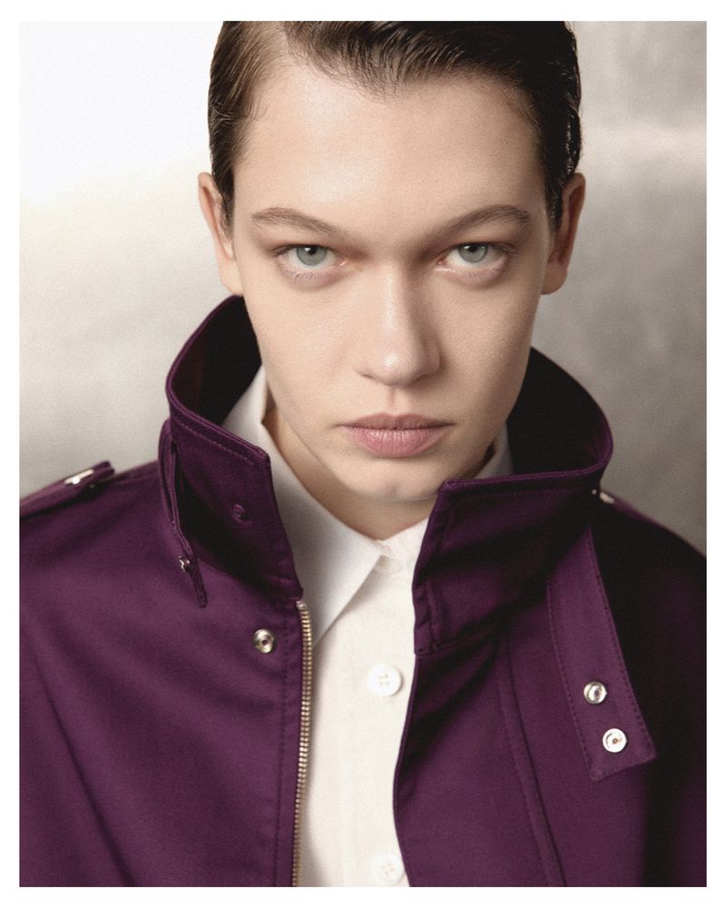 Close-up portrait of a person with short, dark hair wearing a purple jacket and a white shirt in a photo studio setting.