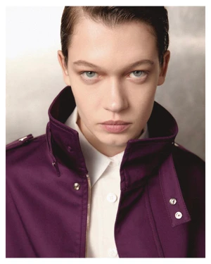 Close-up portrait of a model wearing a purple jacket with a high collar over a white collared shirt against a neutral studio background