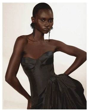 Model wearing a black strapless gown with textured black earrings against a plain white background