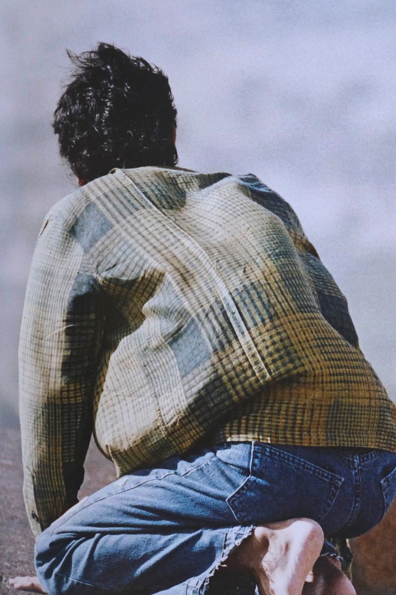 Man kneeling outdoors wearing a plaid shirt and blue jeans viewed from behind