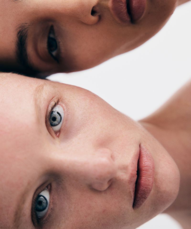 Close-up portrait of two female models with natural skin and neutral expressions against a clean white background.