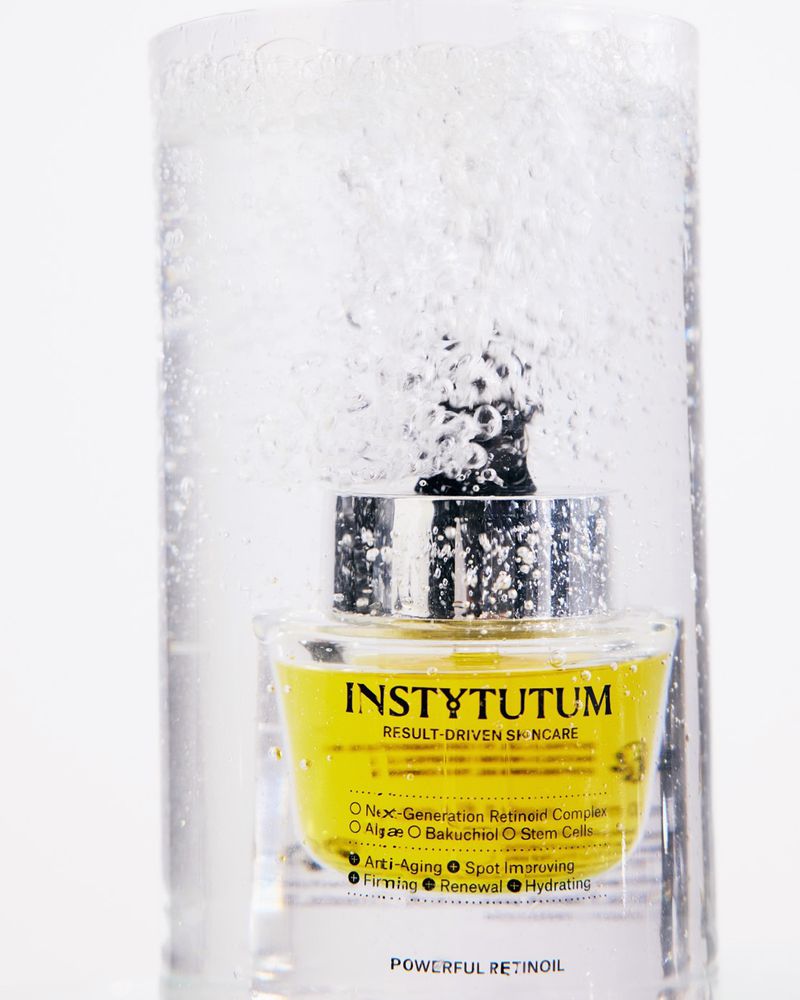 Instytutum skincare dropper bottle submerged behind a tall glass of sparkling water against a white background