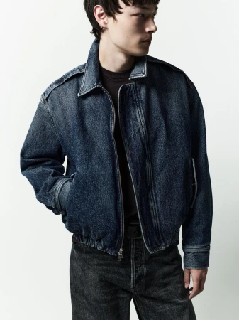 Model wearing a dark denim jacket and black jeans against a white seamless background for AGOLDE Man Spring 2026