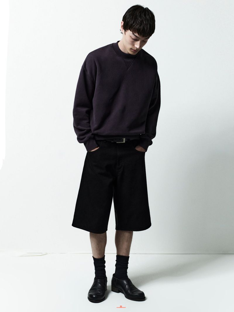 Model wearing dark sweatshirt and black shorts against a white background for AGOLDE Man Spring 2026