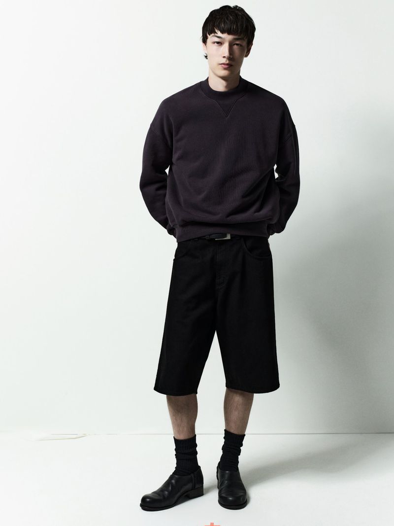 Model wearing dark sweatshirt and black shorts against a white background