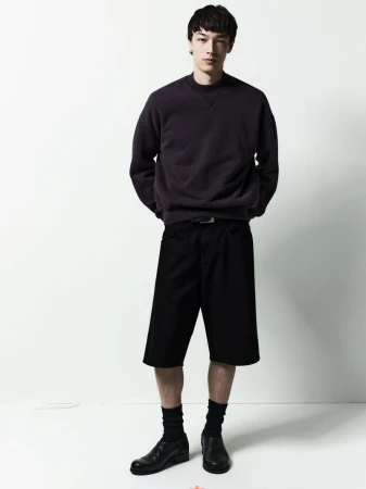 Model wearing dark sweatshirt and black shorts against a white background