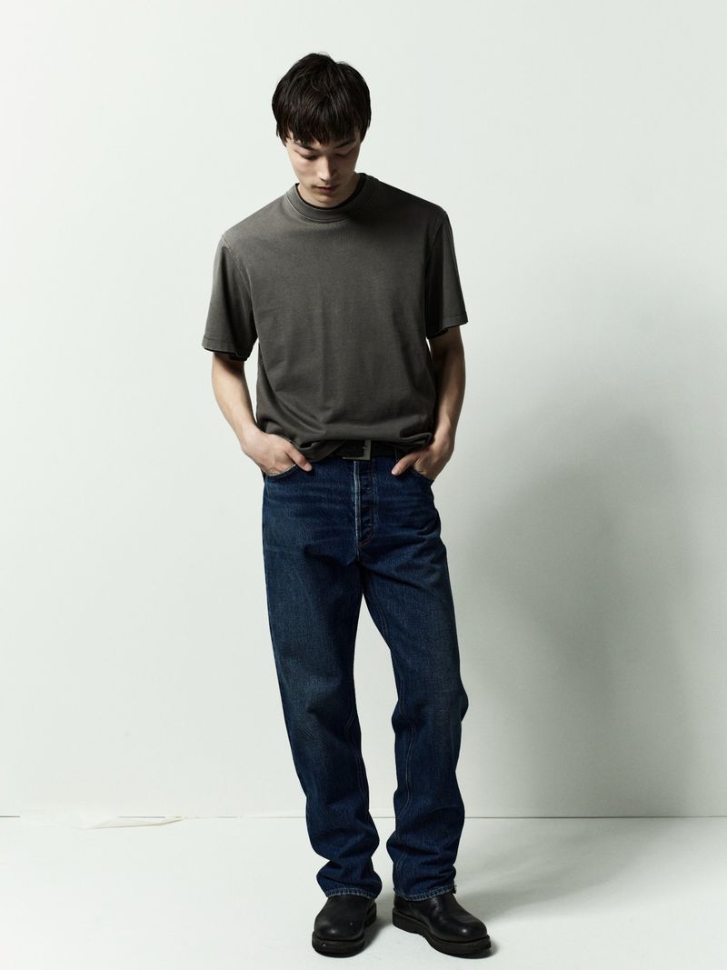 Model wearing a dark grey t-shirt and blue denim jeans against a plain white studio background.