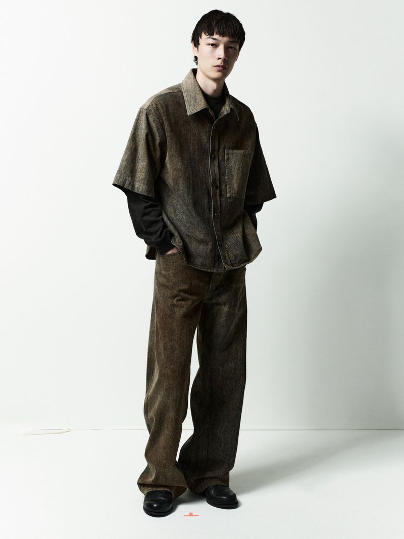Full-length portrait of a male model wearing a short-sleeve button-up shirt and trousers against a clean white backdrop.
