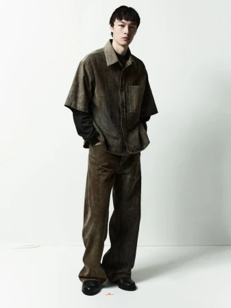 Full-length portrait of a male model wearing a short-sleeve button-up shirt and trousers against a clean white backdrop.
