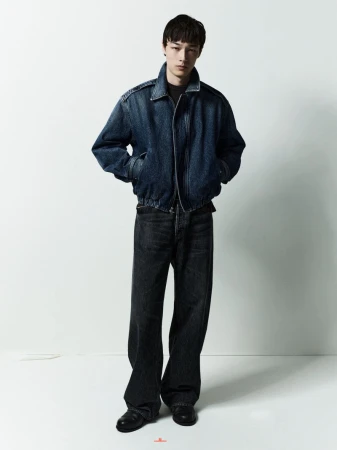 Model standing against a white studio background wearing a dark denim jacket and matching jeans.