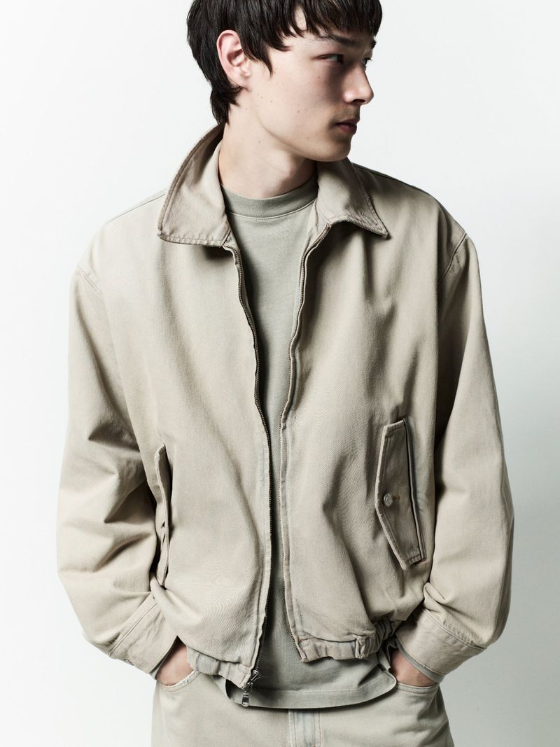 A male model wearing a neutral beige jacket and matching trousers against a solid white background.