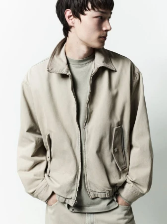 A male model wearing a neutral beige jacket and matching trousers against a solid white background.