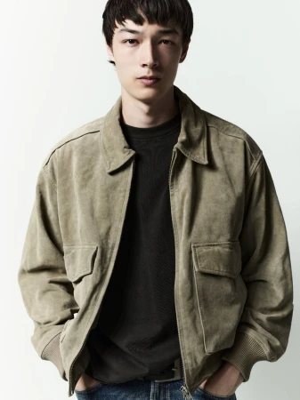 Model wearing a tan suede jacket over a dark t-shirt against a clean white background for AGOLDE Man Spring 2026