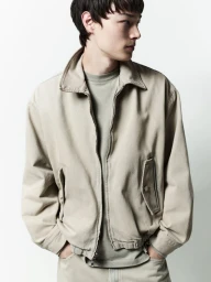 A male model wearing a neutral beige jacket and matching trousers against a solid white background.