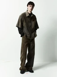 Full-length portrait of a male model wearing a short-sleeve button-up shirt and trousers against a clean white backdrop.