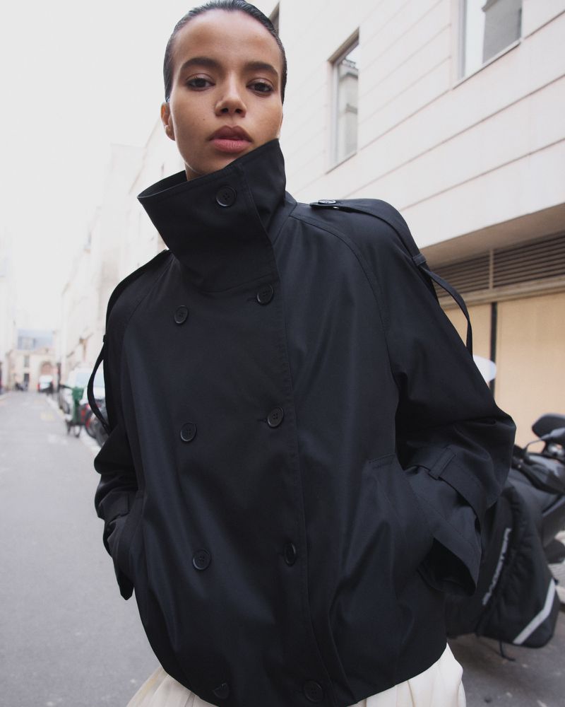 Model wearing a double breasted black jacket outdoors on a city street.