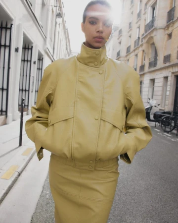 Model wearing a yellow leather jacket and matching skirt standing on a city street.