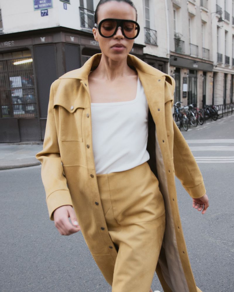 Model in oversized yellow coat and sunglasses walking on a city street for the Coosh project