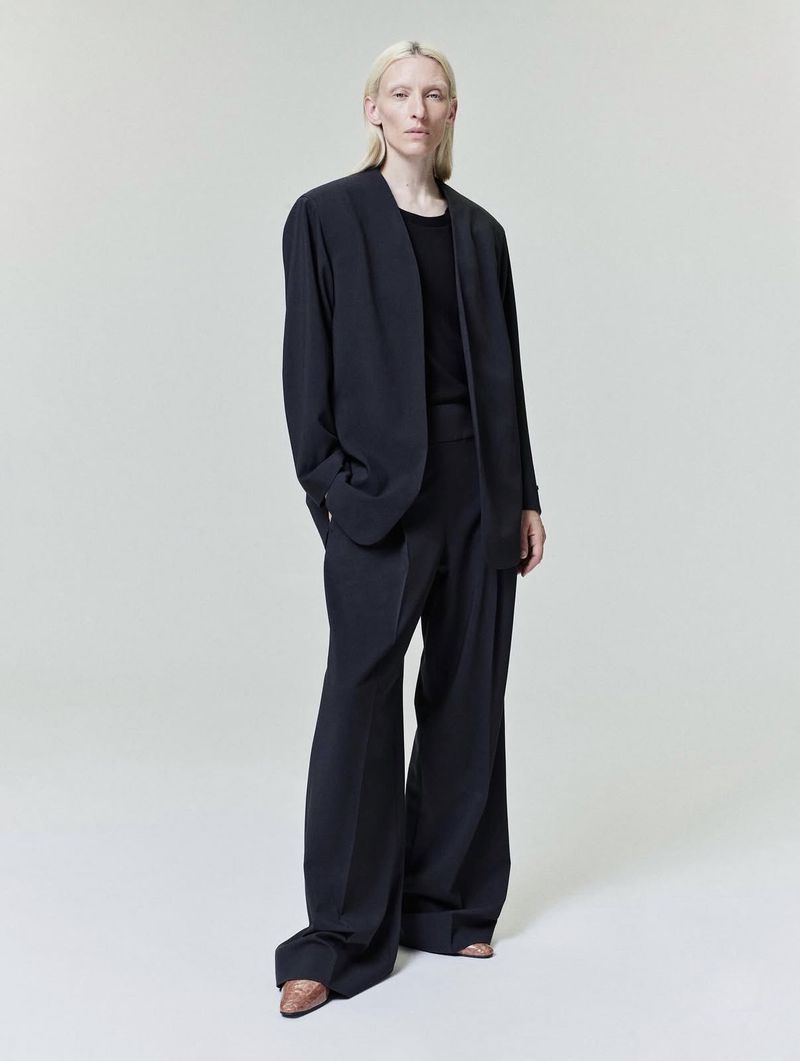 Model Maggie Maurer wearing a dark oversized blazer and trousers against a neutral studio backdrop