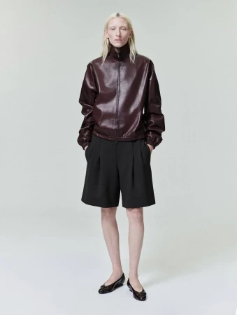 Model with blonde hair wearing a burgundy zip-up jacket and black shorts against a white backdrop.
