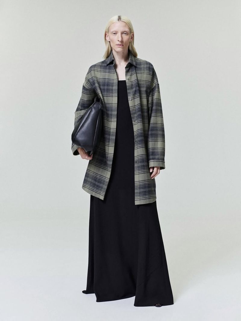 Model Maggie Maurer wearing a plaid shirt and black dress holding a handbag for Fear of God Collection Nine