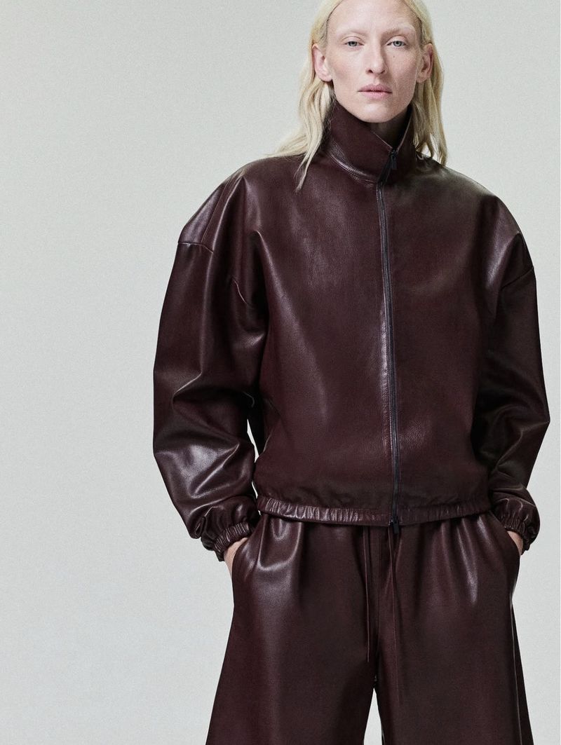 Model Maggie Maurer wearing a burgundy leather zip jacket against a seamless grey background for Fear of God Collection Nine.
