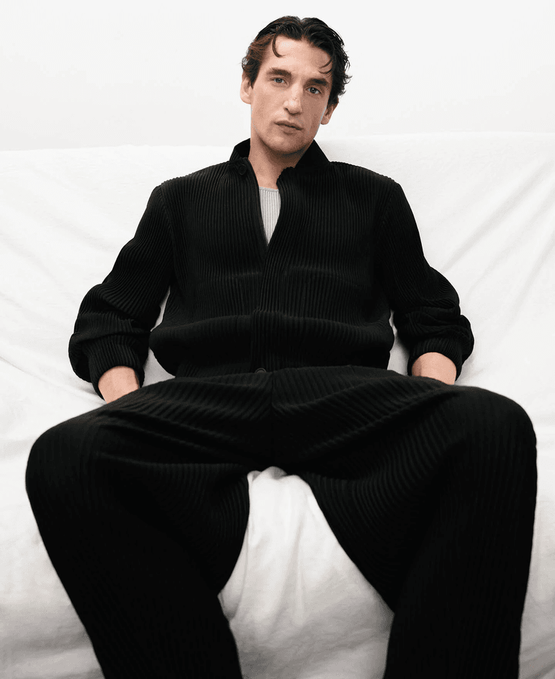 Model Anatol Modzelewski wearing a black ribbed zip cardigan and matching pants against a plain white backdrop.