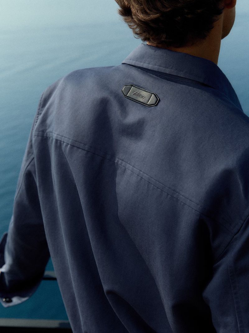 Man wearing a dark blue shirt with a black label on the back yoke, photographed from behind with an ocean background.