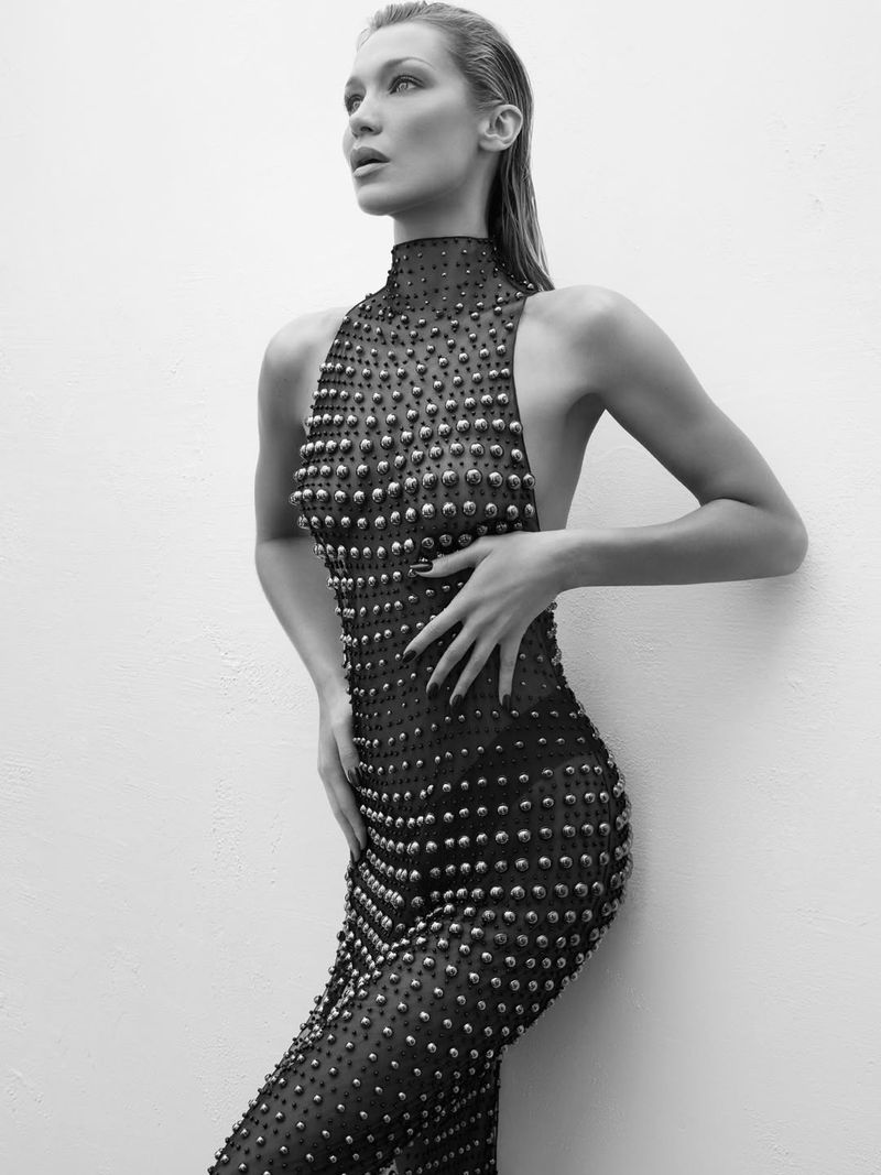 Monochrome portrait of a woman with wet hair wearing a studded dress, standing against a light-colored wall, looking up and to the left.