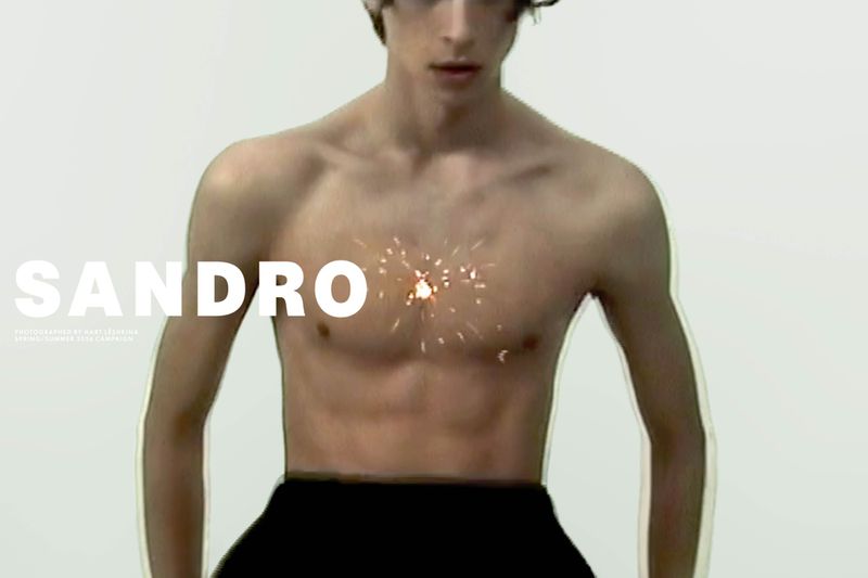 Close-up portrait of a shirtless male model against a plain white seamless studio background for Sandro S/S 2026 campaign.