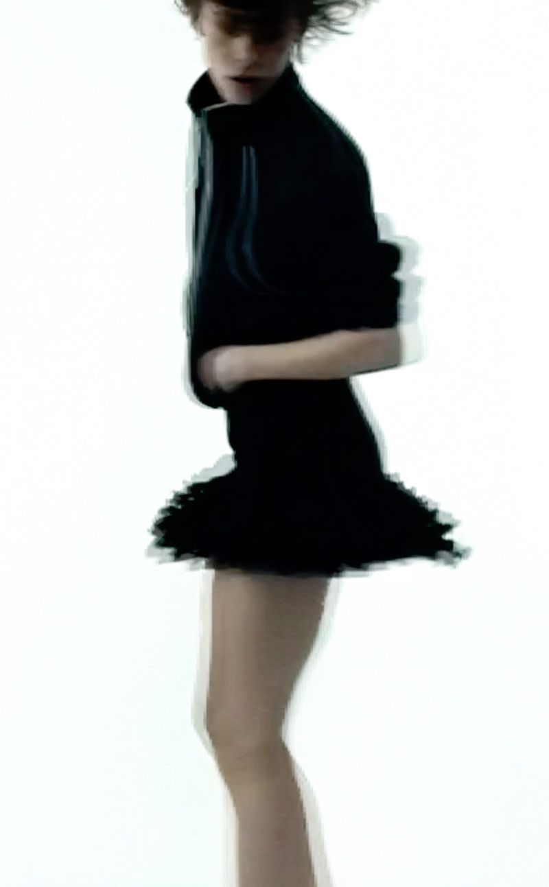 Model in motion wearing a dark jacket and skirt against a bright white background for Sandro