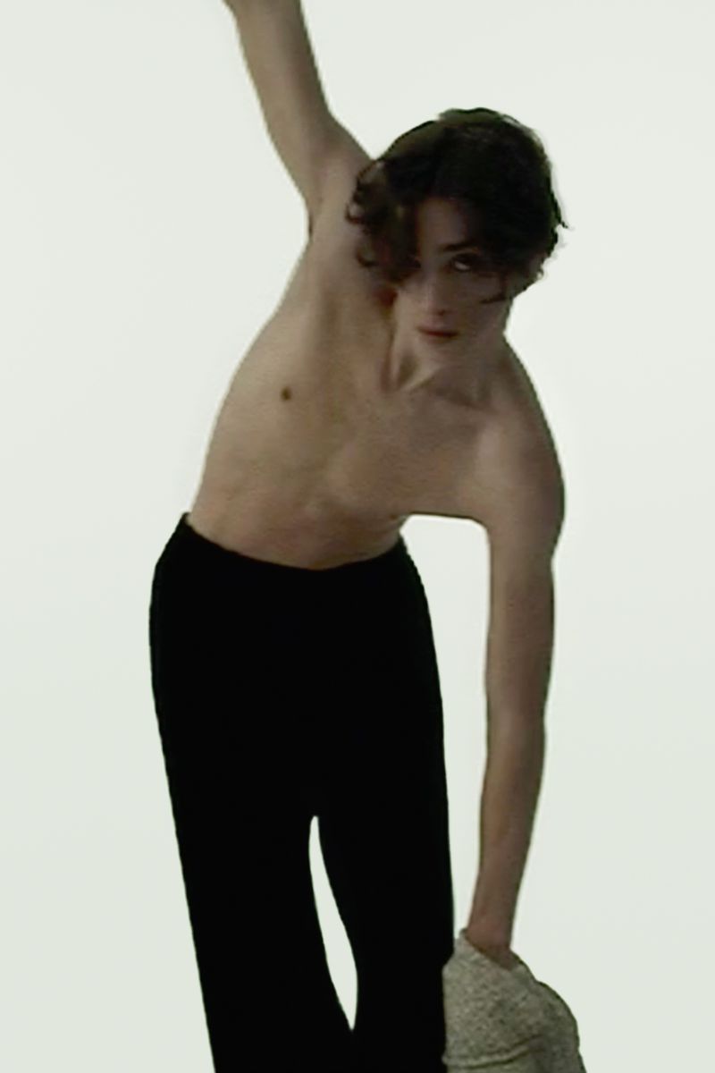 Shirtless male model wearing dark trousers posing dynamically against a white background for the Sandro spring/summer 2026 campaign.
