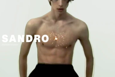 Close-up portrait of a shirtless male model against a plain white seamless studio background for Sandro S/S 2026 campaign.