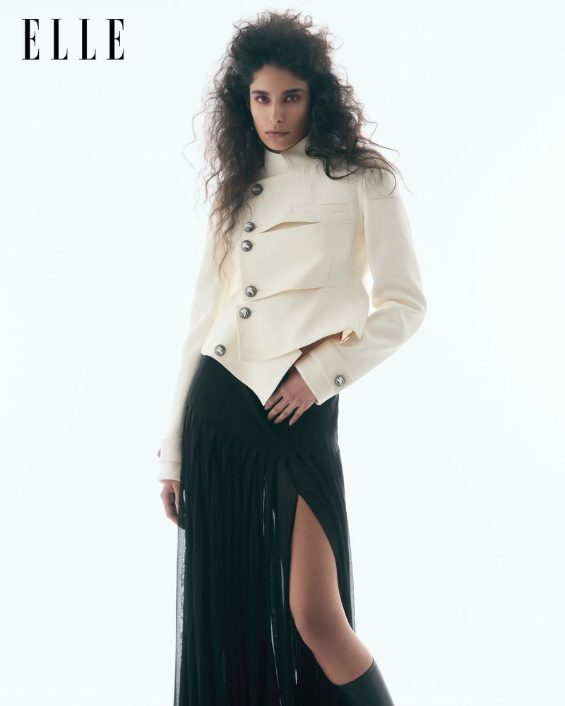 Editorial fashion shot featuring an adult woman in a jacket and skirt against a white background, showcasing fashion and style.