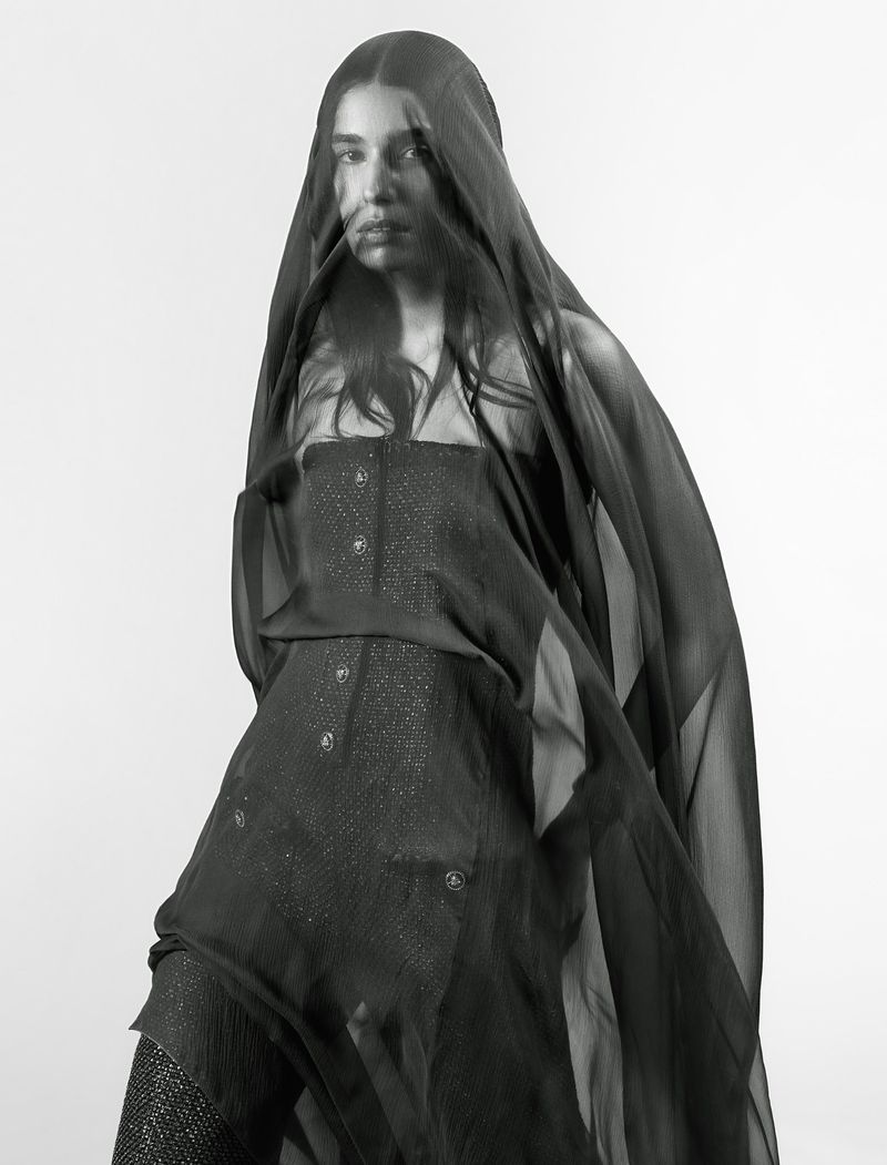 A striking portrait shows a young woman draped in a sheer black fabric, her eyes visible beneath the veil, set against a light background.